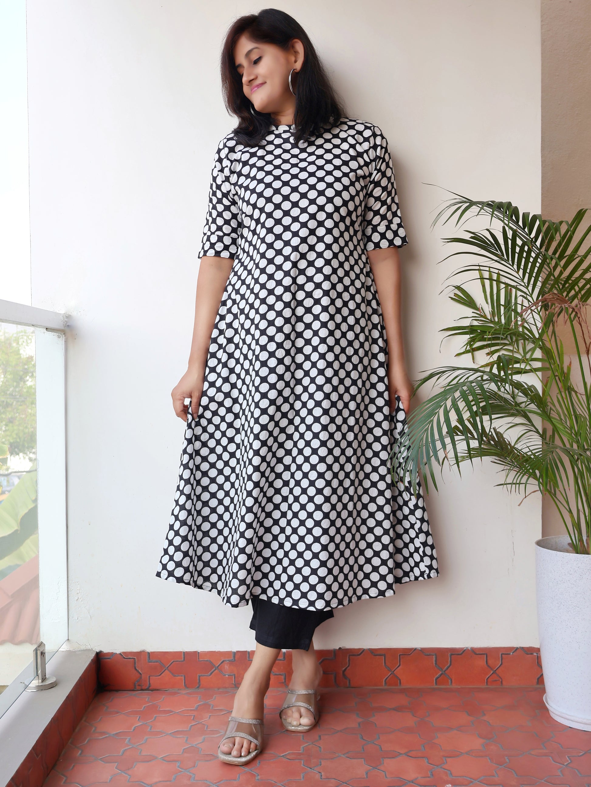 Woman wearing a black and white patterned stylish  kurta standing indoors with a plant in the background.