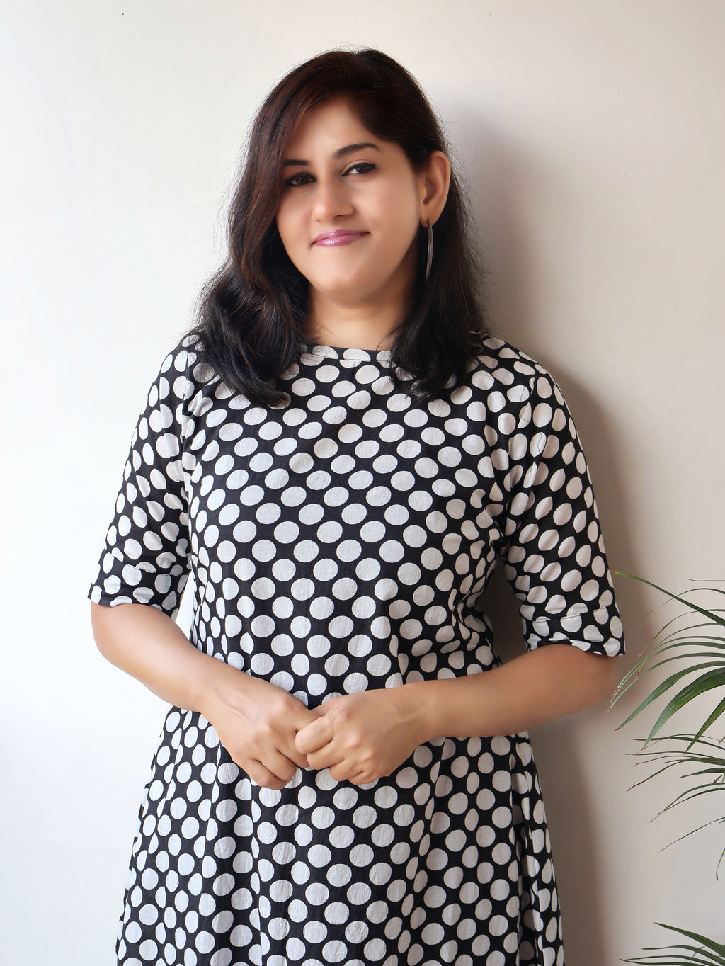 Woman wearing a black and white polka dot dress against a plain background