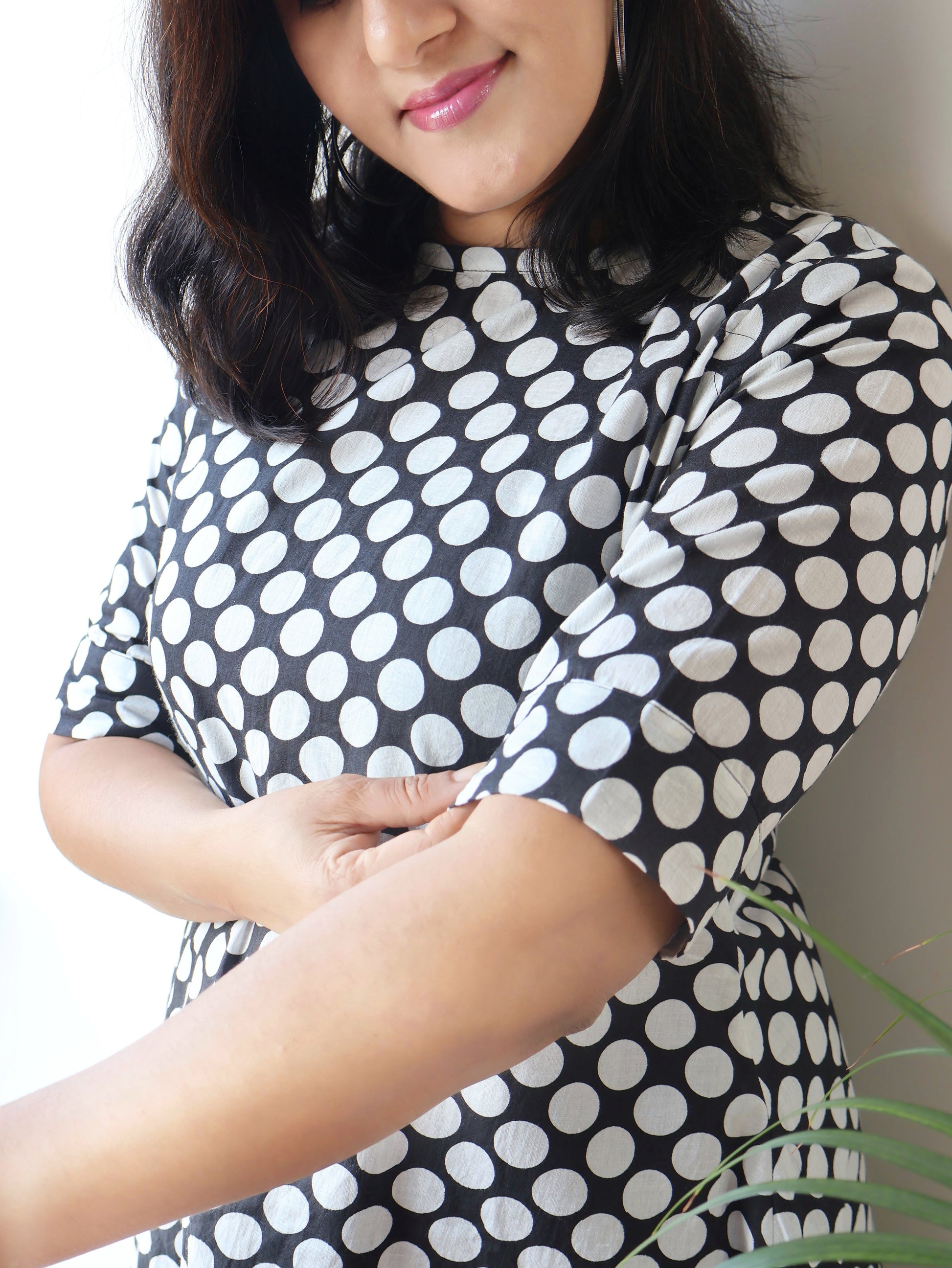 Woman wearing a black and white polka dot dress with a neutral background