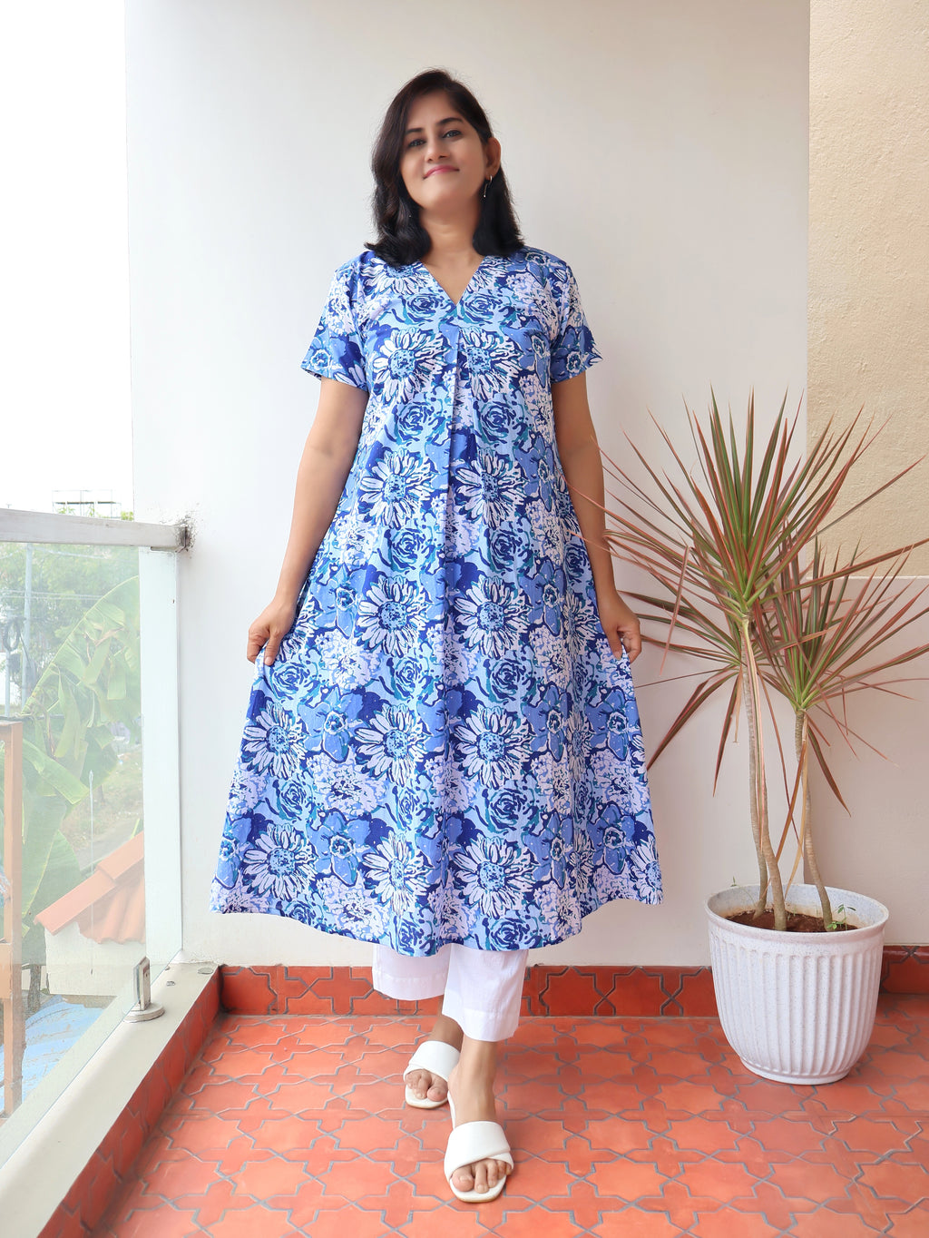 Woman wearing a blue floral dress standing on a balcony with a plant in the background