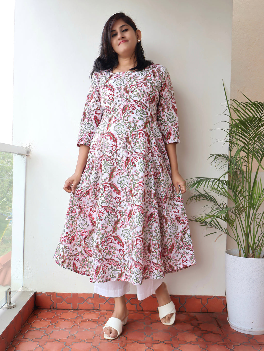 Woman wearing a floral kurta standing indoors with a plant and window in the background