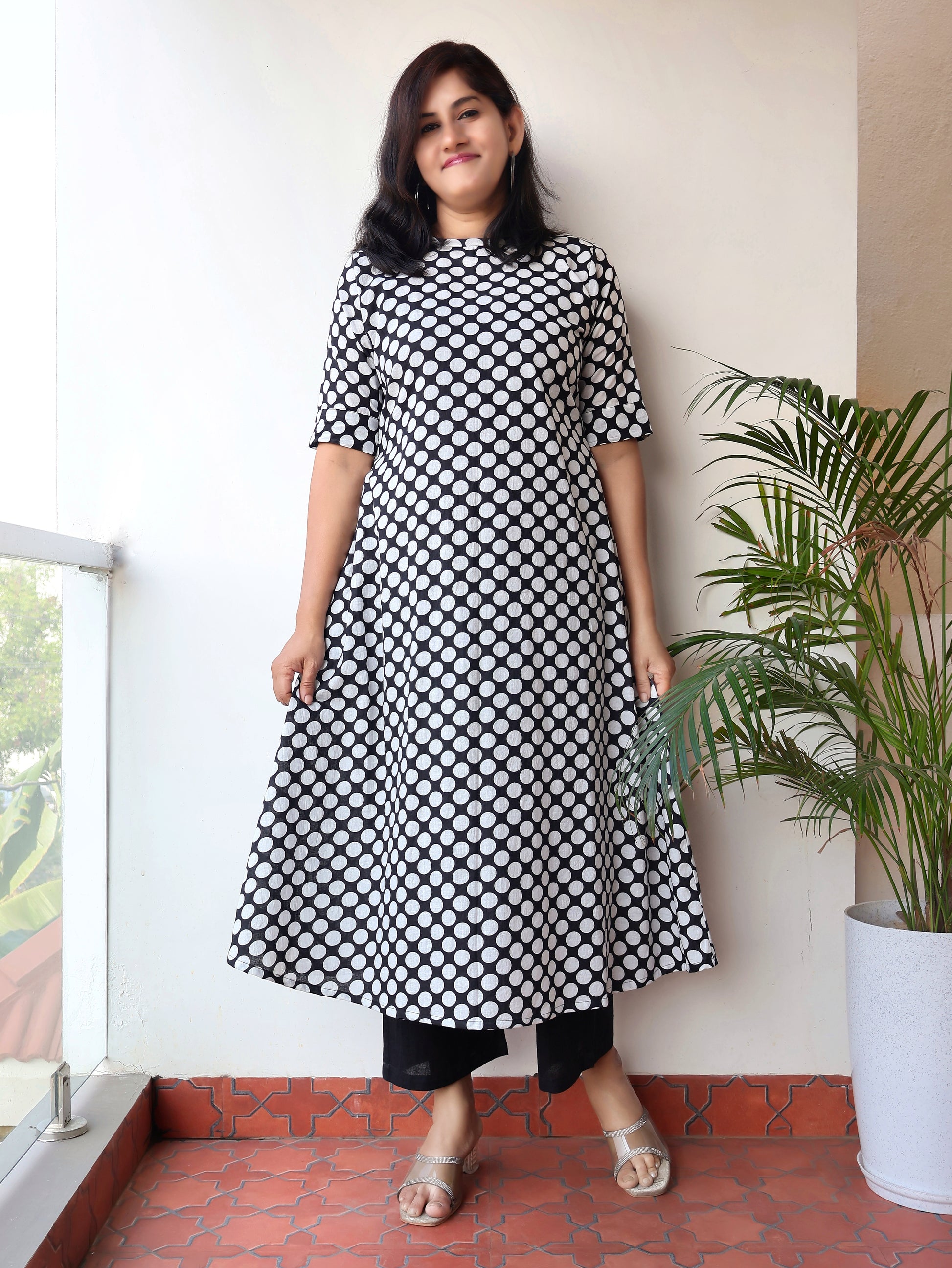 Woman wearing a black and white polka dot dress standing on a balcony with a plant in the background.