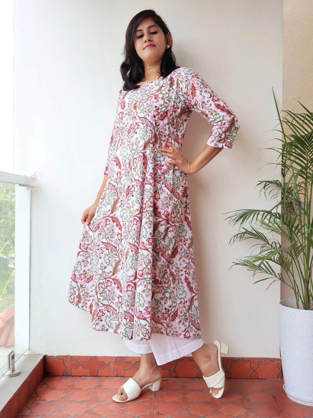 Woman wearing a floral kurta standing indoors with a plant and window in the background