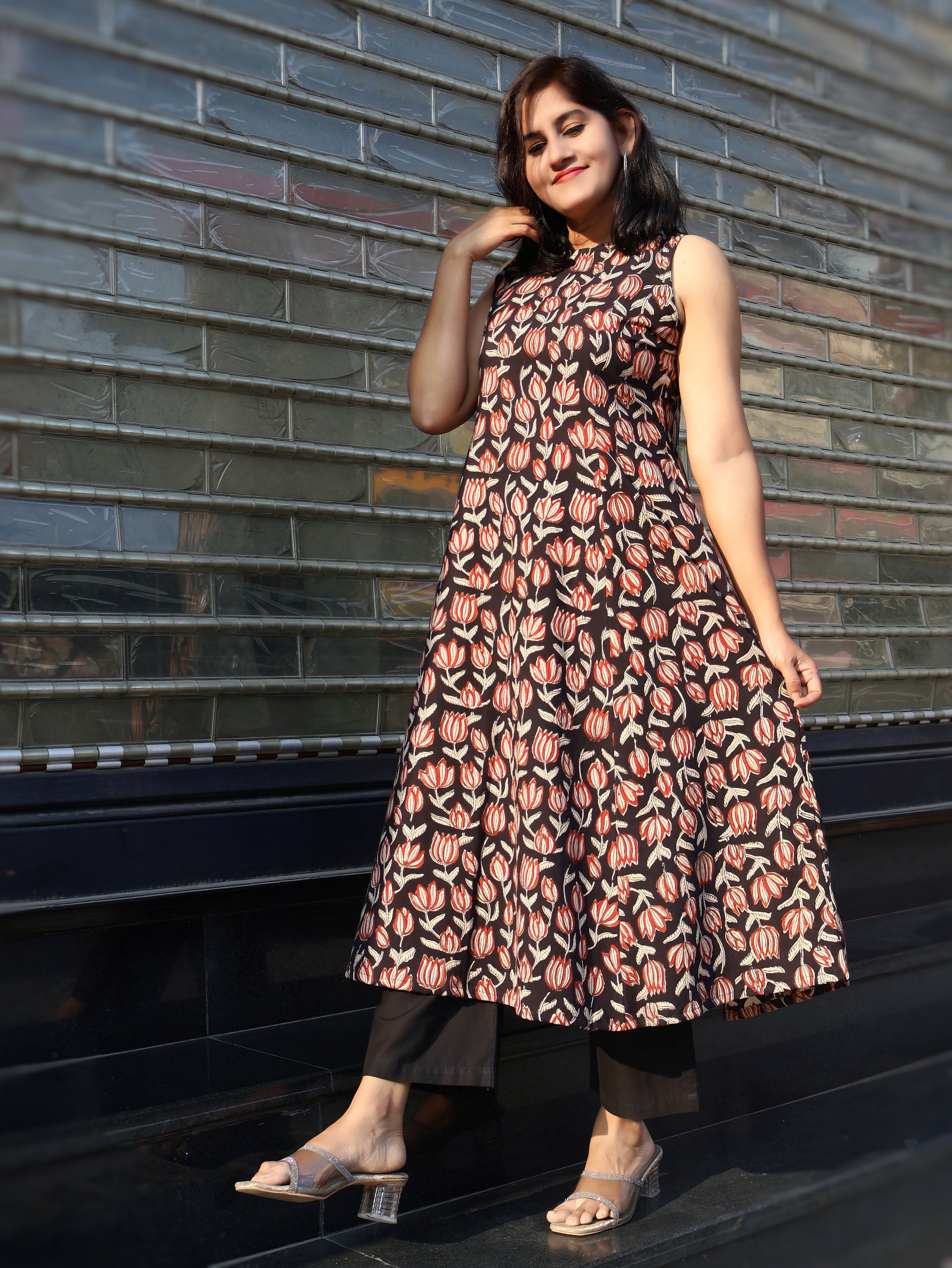 Woman wearing a black sleeveless kurta with black pant, standing against a brick wall.