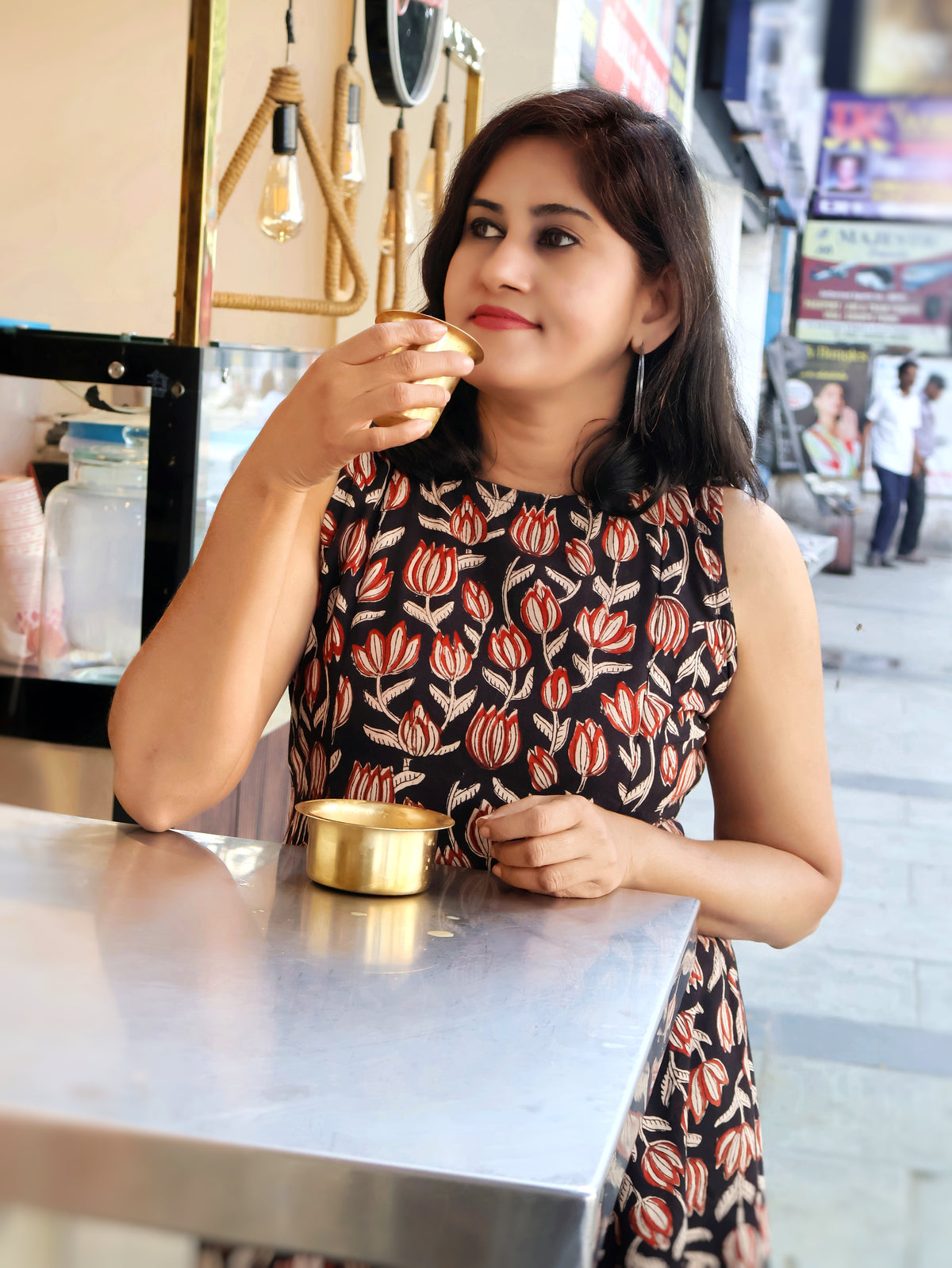Woman having traditional south indian filter coffee, wearing beautiful floral printed bagru sleeveless kurta  in a cafe setting