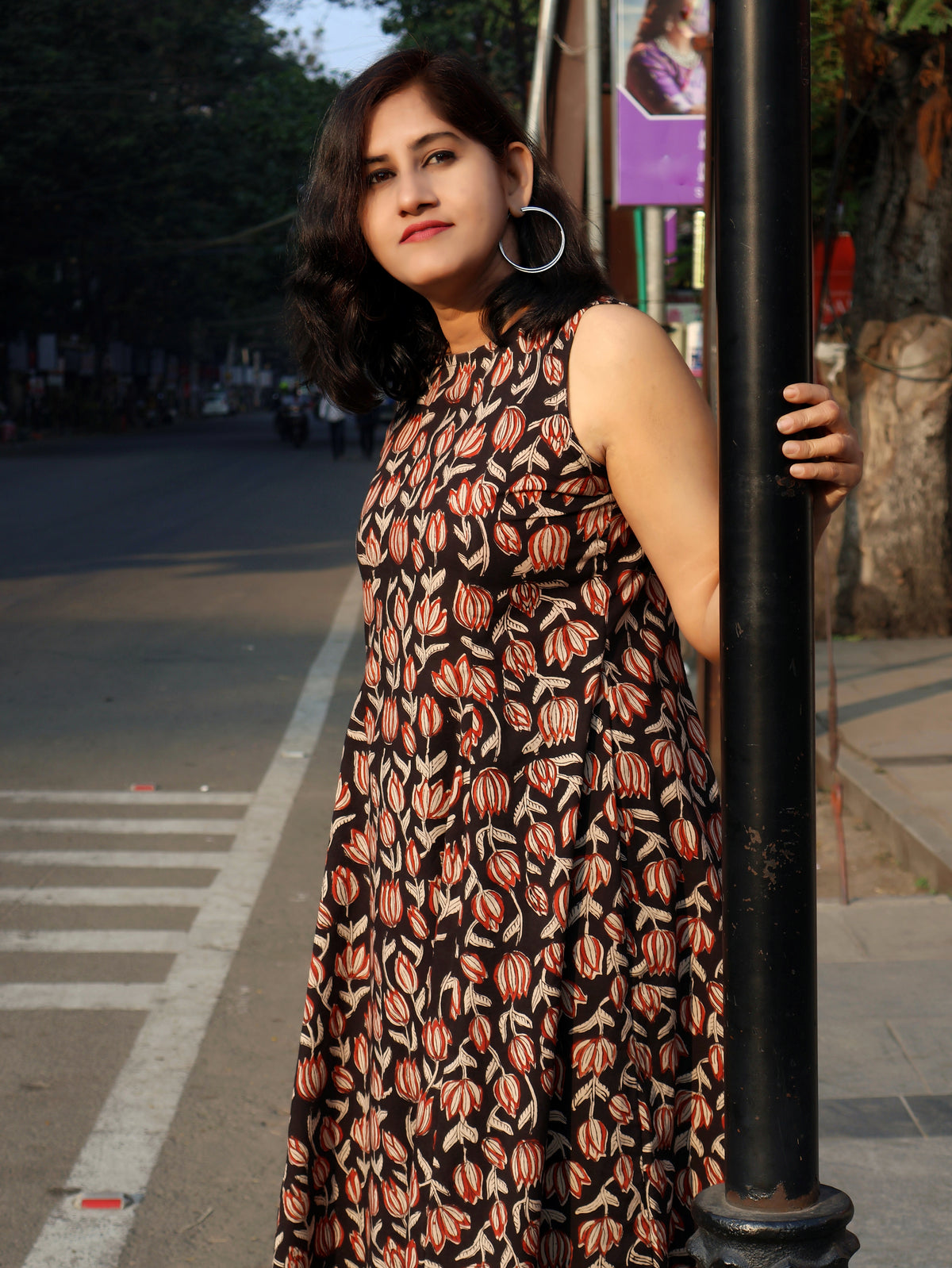 Woman in a black floral kurta  leaning against a pole on a street.