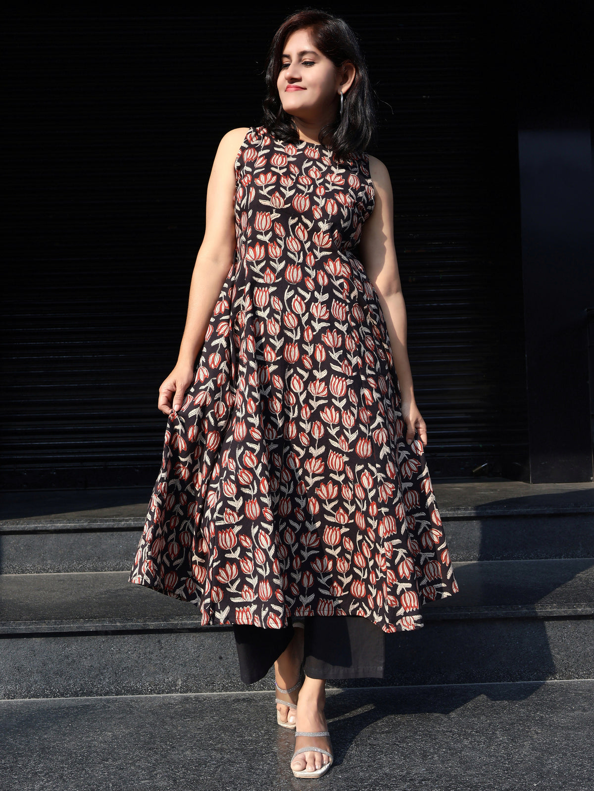 Woman wearing a Bagru Hand Block Floral  sleeveless stylish cotton kurta, standing on steps with a dark background