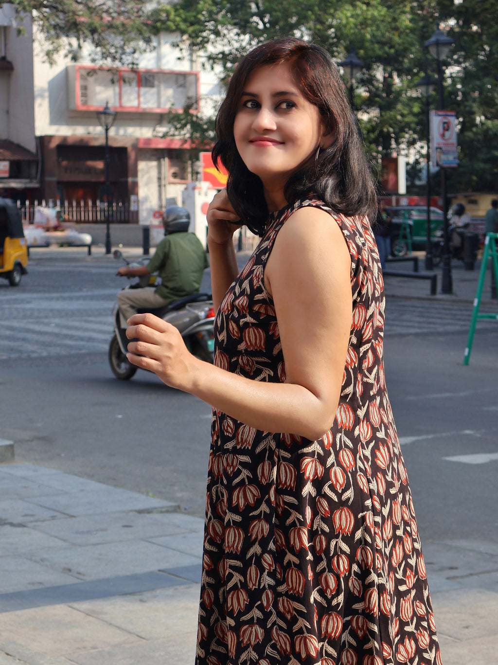 Woman in a black sleeveless red floral kurta with smile, standing on a street with a blurred background