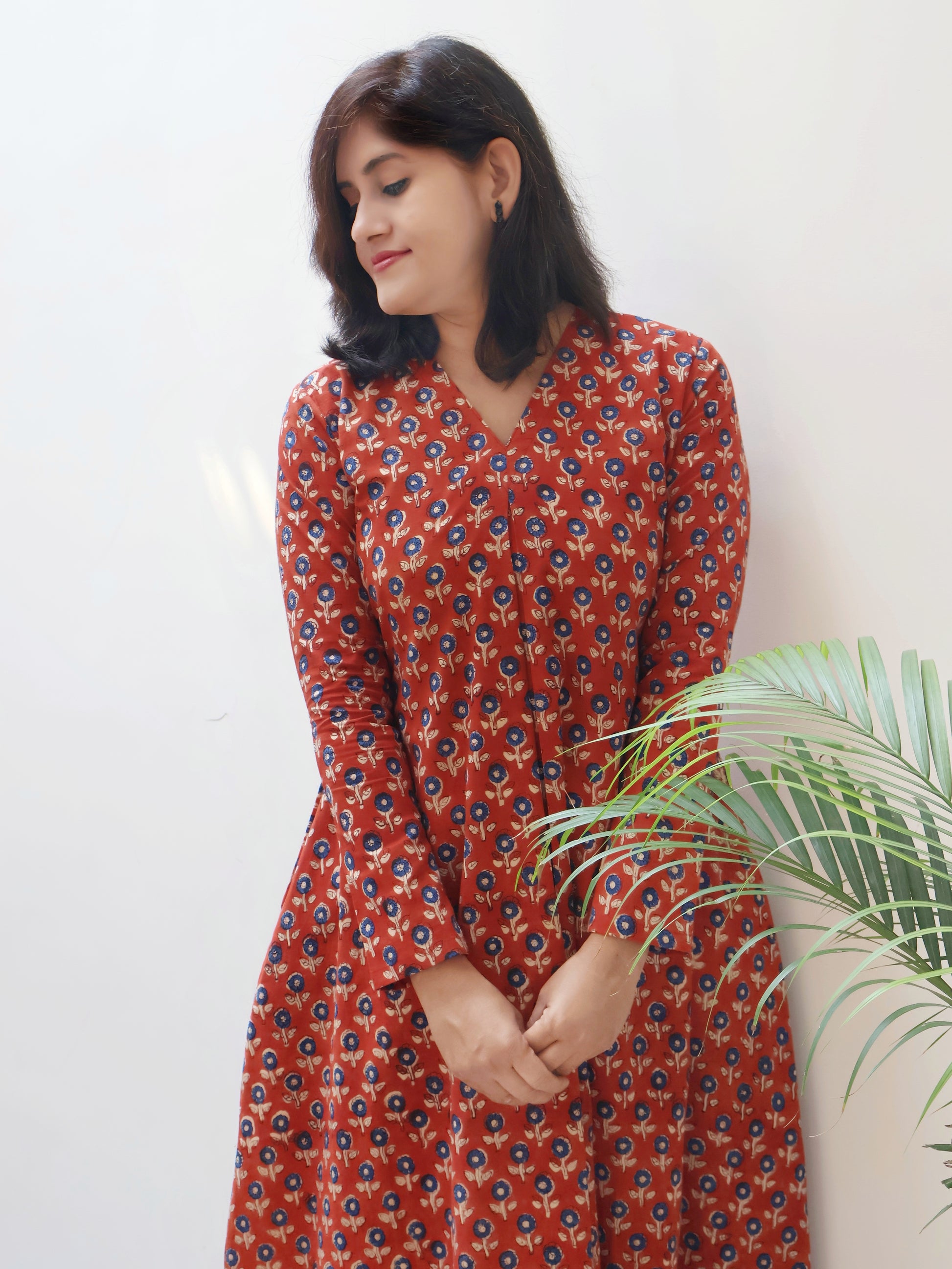 Woman wearing a red floral dress standing next to a plant against a white wall